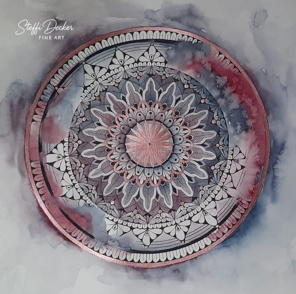 Ein kunstvoll ausgearbeitetes Mandala mit mehreren symmetrischen Ebenen aus blatt‑, tropfen‑ und fächerförmigen Mustern, gestaltet in Rosa‑, Blau‑, Grau‑ und Weißtönen; ein metallisch schimmernder Ring umrahmt die Kreisstruktur, während der Hintergrund in wolkigen Aquarellverläufen aus Grau, Blau und Rosé gehalten ist.